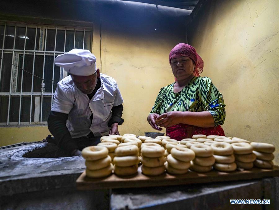 Yusup Tapuhan (L) and his wife bake butter naan in Yuli County of the Mongolian Autonomous Prefecture of Bayingolin, northwest China\'s Xinjiang Uygur Autonomous Region, Oct. 17, 2018. Yusup Tapuhan launched his butter naan business in 2000. The making of this popular pastry has been a tradition in Yuli County. In 2017, a dedicated local naan guild was established to help those in the business optimize profit. Yusup, who is 63, became one of the guild\'s earliest members. With the help of his family, Yusup can make 50 kilograms of butter naan and earn 500 yuan (72 U.S. dollars) a day. (Xinhua/Zhao Ge)