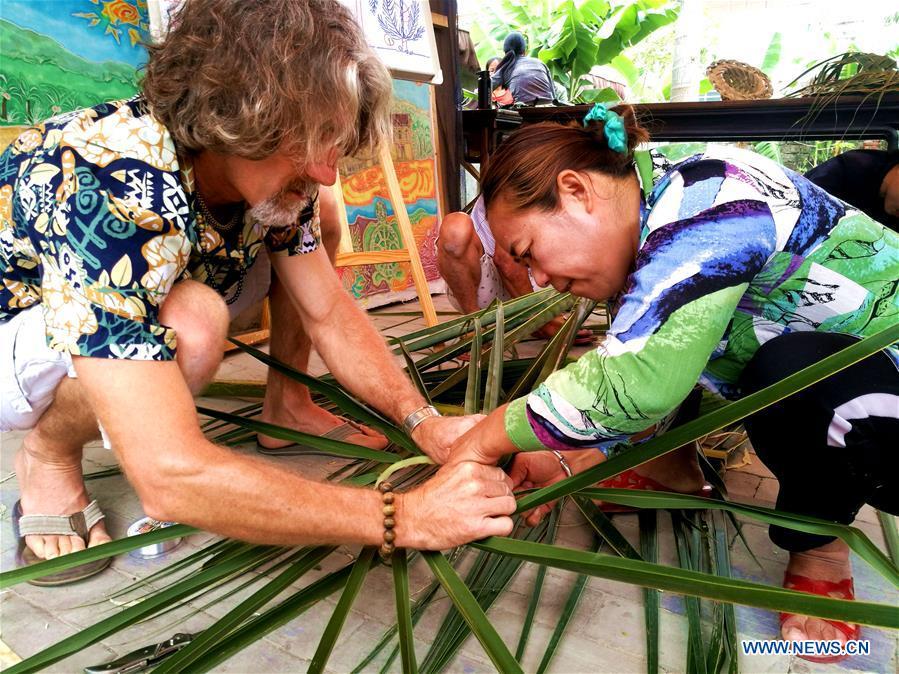 Canadian Craig Anderson (L) teaches a local resident to make artwork on the West Island in Sanya, south China\'s Hainan Province, April 8, 2018. Anderson arrived in February at the West Island inhabited by around 4,000 people. Locals regarded Anderson as a scavenger when he first arrived, as he wandered around the beach almost every day, picking up driftwood, plastic bottles, shattered glasses, and rusty pieces of iron. As time went by, the locals realized that Anderson is an artist who devotes himself in environment protection art design. He profits the recyclable and regenerative materials in making art works. (Xinhua/Yang Guanyu)