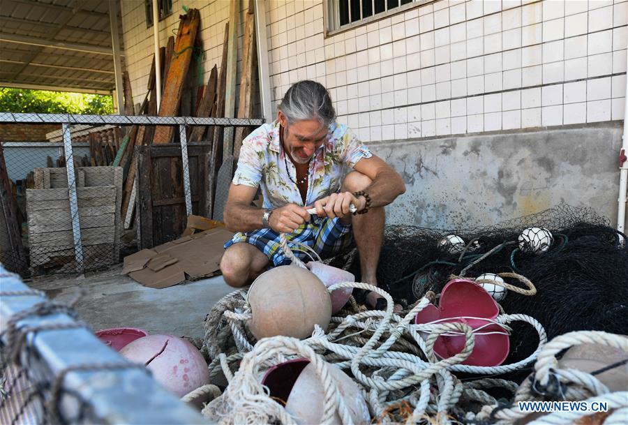 Canadian Craig Anderson arranges recyclable materials at the eco-sustainability service center of the West Island in Sanya, south China\'s Hainan Province, Sept. 19, 2018. Anderson arrived in February at the West Island inhabited by around 4,000 people. Locals regarded Anderson as a scavenger when he first arrived, as he wandered around the beach almost every day, picking up driftwood, plastic bottles, shattered glasses, and rusty pieces of iron. As time went by, the locals realized that Anderson is an artist who devotes himself in environment protection art design. He profits the recyclable and regenerative materials in making art works. (Xinhua/Yang Guanyu)