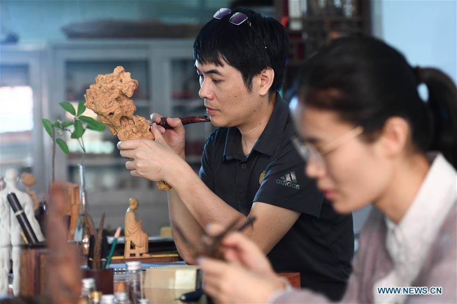 Lin Jianjun (L) and Chen Qin make wood carving at their studio in Putian, southeast China\'s Fujian Province, Oct. 24, 2018. Lin Jianjun, who learnt wood carving at the age of 16, has studied the making skill of this traditional artwork for more than 20 years. In 2014, Lin got married with Chen Qin. The wife was influenced by her husband and got interested in wood carving. She developed the wood carving by combining a traditional skill to make wood carving inlaid with gold and silver. The couple meanwhile try to promote the Putian wood carving by giving lessons, instructing apprentices and displaying their works to the public. In 2018, Lin was appointed as the inheritor of the wood carving skill, a provincial-level intangible cultural heritage. (Xinhua/Zhang Guojun)