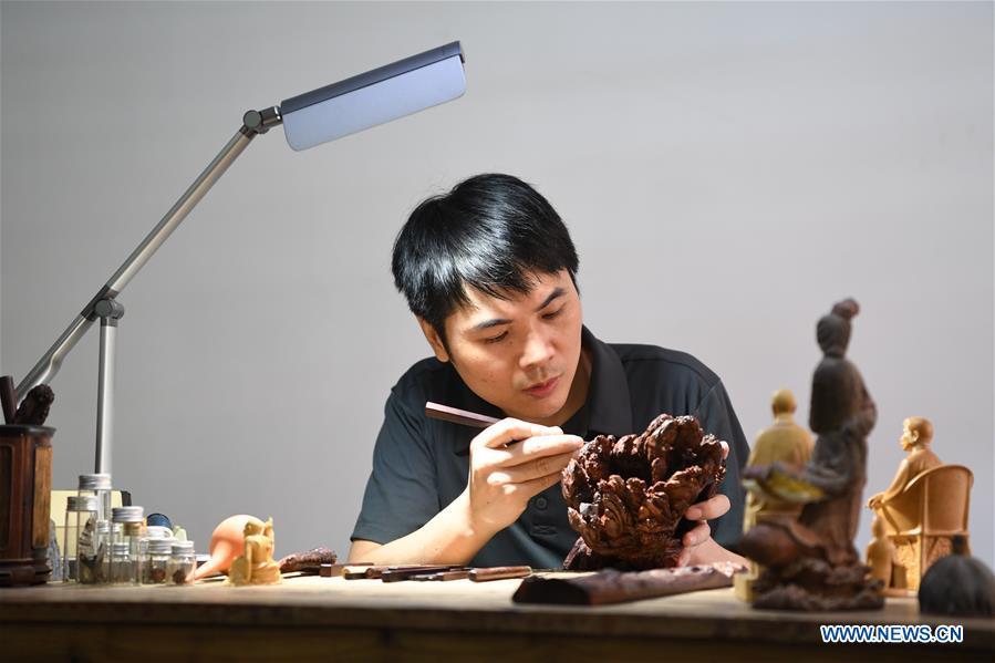 Lin Jianjun makes wood carving at a studio in Putian, southeast China\'s Fujian Province, Oct. 23, 2018. Lin Jianjun, who learnt wood carving at the age of 16, has studied the making skill of this traditional artwork for more than 20 years. In 2014, Lin got married with Chen Qin. The wife was influenced by her husband and got interested in wood carving. She developed the wood carving by combining a traditional skill to make wood carving inlaid with gold and silver. The couple meanwhile try to promote the Putian wood carving by giving lessons, instructing apprentices and displaying their works to the public. In 2018, Lin was appointed as the inheritor of the wood carving skill, a provincial-level intangible cultural heritage. (Xinhua/Jiang Kehong)