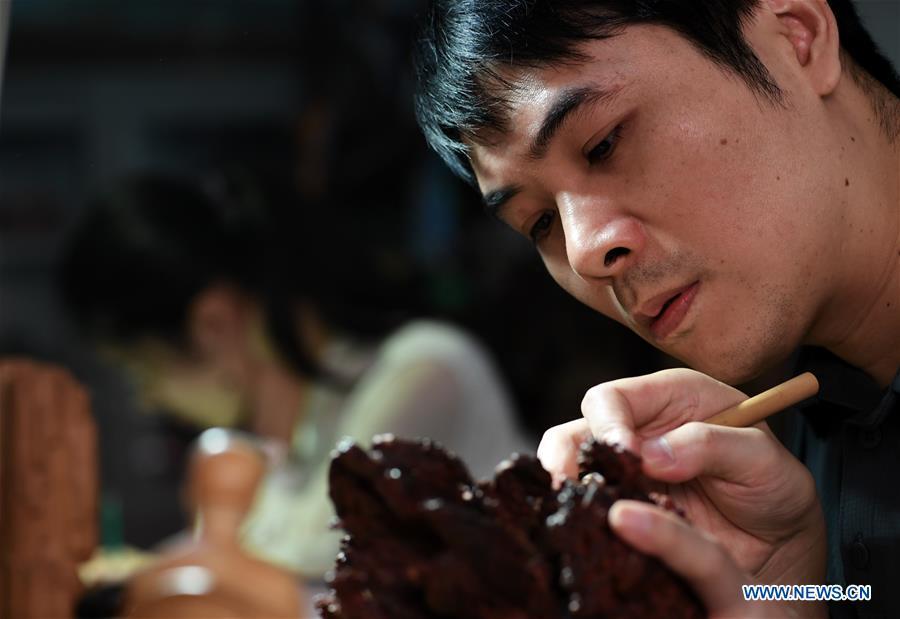 Lin Jianjun makes wood carving at a studio in Putian, southeast China\'s Fujian Province, Oct. 23, 2018. Lin Jianjun, who learnt wood carving at the age of 16, has studied the making skill of this traditional artwork for more than 20 years. In 2014, Lin got married with Chen Qin. The wife was influenced by her husband and got interested in wood carving. She developed the wood carving by combining a traditional skill to make wood carving inlaid with gold and silver. The couple meanwhile try to promote the Putian wood carving by giving lessons, instructing apprentices and displaying their works to the public. In 2018, Lin was appointed as the inheritor of the wood carving skill, a provincial-level intangible cultural heritage. (Xinhua/Zhang Guojun)