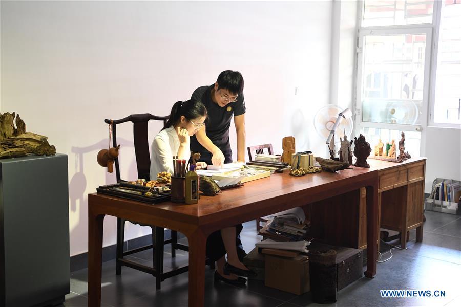 Lin Jianjun (R) and Chen Qin discuss the design of wood carving ornament at their studio in Putian, southeast China\'s Fujian Province, Oct. 23, 2018. Lin Jianjun, who learnt wood carving at the age of 16, has studied the making skill of this traditional artwork for more than 20 years. In 2014, Lin got married with Chen Qin. The wife was influenced by her husband and got interested in wood carving. She developed the wood carving by combining a traditional skill to make wood carving inlaid with gold and silver. The couple meanwhile try to promote the Putian wood carving by giving lessons, instructing apprentices and displaying their works to the public. In 2018, Lin was appointed as the inheritor of the wood carving skill, a provincial-level intangible cultural heritage. (Xinhua/Jiang Kehong)