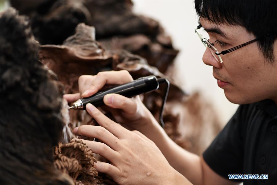 Lin Jianjun makes wood carving at a studio in Putian, southeast China\'s Fujian Province, Oct. 23, 2018. Lin Jianjun, who learnt wood carving at the age of 16, has studied the making skill of this traditional artwork for more than 20 years. In 2014, Lin got married with Chen Qin. The wife was influenced by her husband and got interested in wood carving. She developed the wood carving by combining a traditional skill to make wood carving inlaid with gold and silver. The couple meanwhile try to promote the Putian wood carving by giving lessons, instructing apprentices and displaying their works to the public. In 2018, Lin was appointed as the inheritor of the wood carving skill, a provincial-level intangible cultural heritage. (Xinhua/Zhang Guojun)
