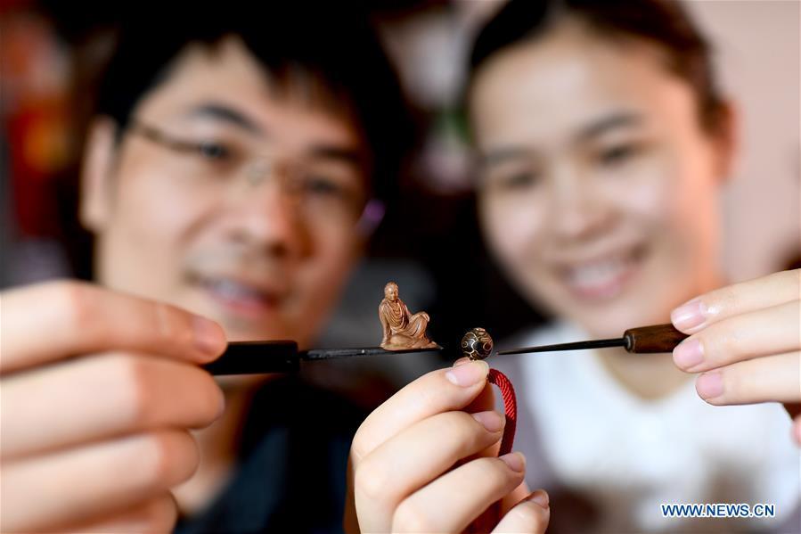 Lin Jianjun (L) and Chen Qin show wood carving at their studio in Putian, southeast China\'s Fujian Province, Oct. 24, 2018. Lin Jianjun, who learnt wood carving at the age of 16, has studied the making skill of this traditional artwork for more than 20 years. In 2014, Lin got married with Chen Qin. The wife was influenced by her husband and got interested in wood carving. She developed the wood carving by combining a traditional skill to make wood carving inlaid with gold and silver. The couple meanwhile try to promote the Putian wood carving by giving lessons, instructing apprentices and displaying their works to the public. In 2018, Lin was appointed as the inheritor of the wood carving skill, a provincial-level intangible cultural heritage.(Xinhua/Jiang Kehong)