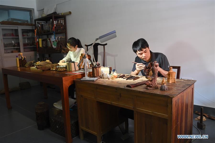 Lin Jianjun (R) and Chen Qin make wood carving at their studio in Putian, southeast China\'s Fujian Province, Oct. 23, 2018. Lin Jianjun, who learnt wood carving at the age of 16, has studied the making skill of this traditional artwork for more than 20 years. In 2014, Lin got married with Chen Qin. The wife was influenced by her husband and got interested in wood carving. She developed the wood carving by combining a traditional skill to make wood carving inlaid with gold and silver. The couple meanwhile try to promote the Putian wood carving by giving lessons, instructing apprentices and displaying their works to the public. In 2018, Lin was appointed as the inheritor of the wood carving skill, a provincial-level intangible cultural heritage. (Xinhua/Jiang Kehong)