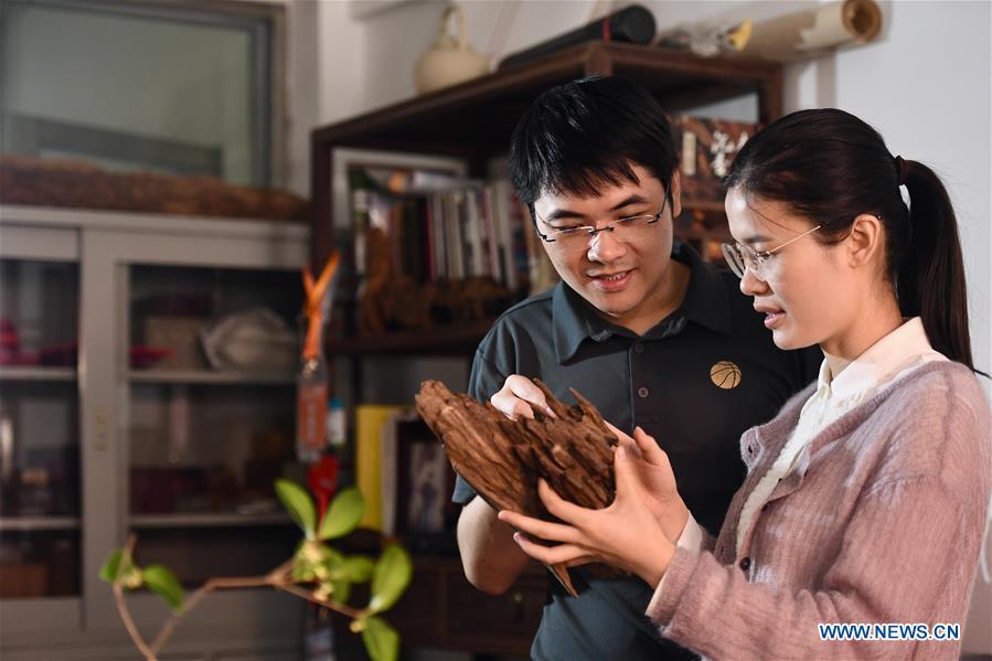 Lin Jianjun (L) and Chen Qin discuss the design of wood carving ornament at their studio in Putian, southeast China\'s Fujian Province, Oct. 24, 2018. Lin Jianjun, who learnt wood carving at the age of 16, has studied the making skill of this traditional artwork for more than 20 years. In 2014, Lin got married with Chen Qin. The wife was influenced by her husband and got interested in wood carving. She developed the wood carving by combining a traditional skill to make wood carving inlaid with gold and silver. The couple meanwhile try to promote the Putian wood carving by giving lessons, instructing apprentices and displaying their works to the public. In 2018, Lin was appointed as the inheritor of the wood carving skill, a provincial-level intangible cultural heritage. (Xinhua/Jiang Kehong)