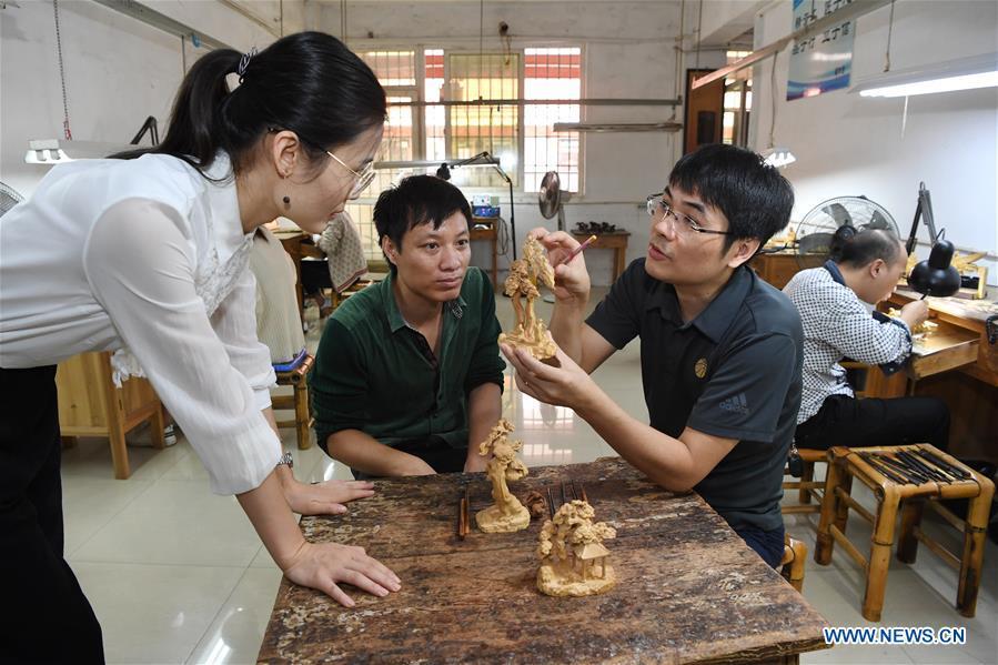 Lin Jianjun (R, front) and Chen Qin check wood carving products at a plant in Putian, southeast China\'s Fujian Province, Oct. 23, 2018. Lin Jianjun, who learnt wood carving at the age of 16, has studied the making skill of this traditional artwork for more than 20 years. In 2014, Lin got married with Chen Qin. The wife was influenced by her husband and got interested in wood carving. She developed the wood carving by combining a traditional skill to make wood carving inlaid with gold and silver. The couple meanwhile try to promote the Putian wood carving by giving lessons, instructing apprentices and displaying their works to the public. In 2018, Lin was appointed as the inheritor of the wood carving skill, a provincial-level intangible cultural heritage. (Xinhua/Jiang Kehong)