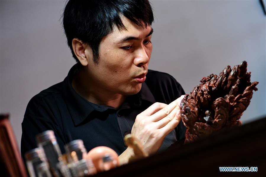 Lin Jianjun makes wood carving at a studio in Putian, southeast China\'s Fujian Province, Oct. 23, 2018. Lin Jianjun, who learnt wood carving at the age of 16, has studied the making skill of this traditional artwork for more than 20 years. In 2014, Lin got married with Chen Qin. The wife was influenced by her husband and got interested in wood carving. She developed the wood carving by combining a traditional skill to make wood carving inlaid with gold and silver. The couple meanwhile try to promote the Putian wood carving by giving lessons, instructing apprentices and displaying their works to the public. In 2018, Lin was appointed as the inheritor of the wood carving skill, a provincial-level intangible cultural heritage. (Xinhua/Zhang Guojun)