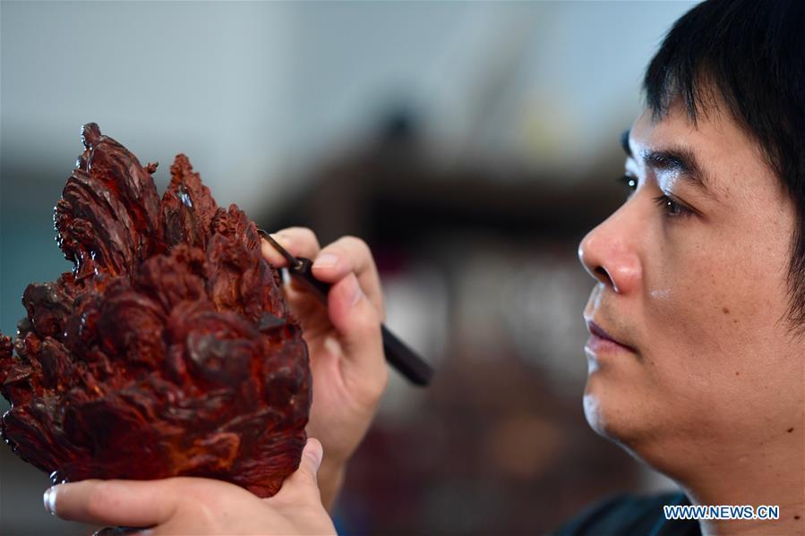 Lin Jianjun makes wood carving at a studio in Putian, southeast China\'s Fujian Province, Oct. 24, 2018. Lin Jianjun, who learnt wood carving at the age of 16, has studied the making skill of this traditional artwork for more than 20 years. In 2014, Lin got married with Chen Qin. The wife was influenced by her husband and got interested in wood carving. She developed the wood carving by combining a traditional skill to make wood carving inlaid with gold and silver. The couple meanwhile try to promote the Putian wood carving by giving lessons, instructing apprentices and displaying their works to the public. In 2018, Lin was appointed as the inheritor of the wood carving skill, a provincial-level intangible cultural heritage.(Xinhua/Jiang Kehong)