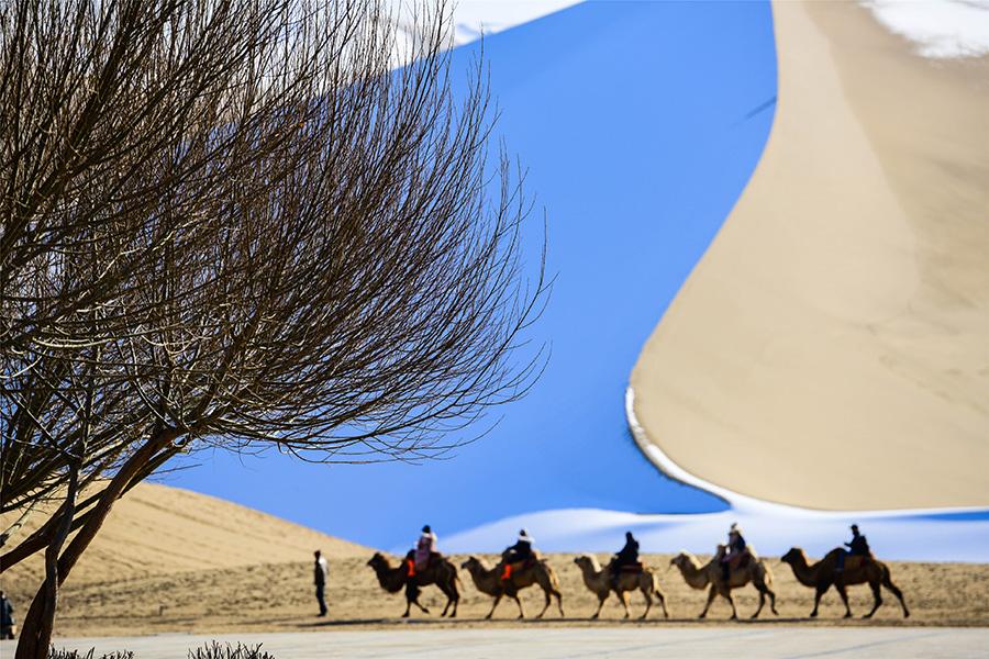 Dunhuang embraces this winter\'s first snowfall on Nov. 14. As the sun comes out, snow scenery in local landmark attractions like the Mingsha Mountain and Yueya Spring, a crescent-shaped spring-fed lake surrounded by desert, turns to a fairyland. (Photo/China Daily)