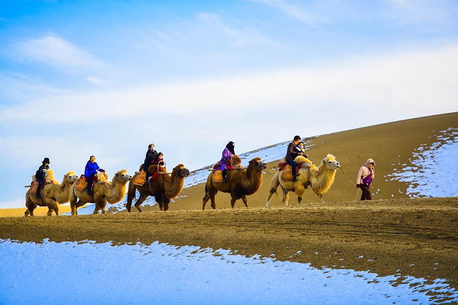 Dunhuang embraces this winter\'s first snowfall on Nov. 14. As the sun comes out, snow scenery in local landmark attractions like the Mingsha Mountain and Yueya Spring, a crescent-shaped spring-fed lake surrounded by desert, turns to a fairyland. (Photo/China Daily)