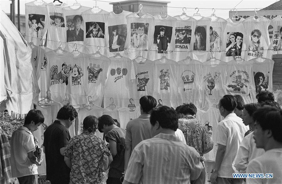File photo issued on July 20, 1992 shows people selecting T-shirt printed with portraits of pop actors and singers in Beijing, capital of China. From 1978 when China started its reform and opening-up policy, a door to the outside world has been opened. Along with the imported commodities, fashion ideas inevitably slipped into China and since then the country, which was somewhat lack of fashion diversity, started its journey to pursue fashions. Over the past four decades, the thirst for beauty has driven Chinese people to pursue every possible fashionable element. The change first came with dress when colorful and diversified clothing prevailed as against the former dominant blue and grey. For a time, men and women raced to hairdressers\' just for trendy hairdos. Eating McDonald\'s or western cuisine even once was regarded as a fashionable thing. However, the most conspicuous change is that Chinese people have become more inclusive and they tend to accept new fashions, styles and concepts. China nowadays is dazzling the world not only on the fashion stage but in many other fields. Changes in fashions, as a profile of society, has well interpreted the benefits to people brought by China\'s reform and opening-up policy. (Xinhua/Zeng Huang)