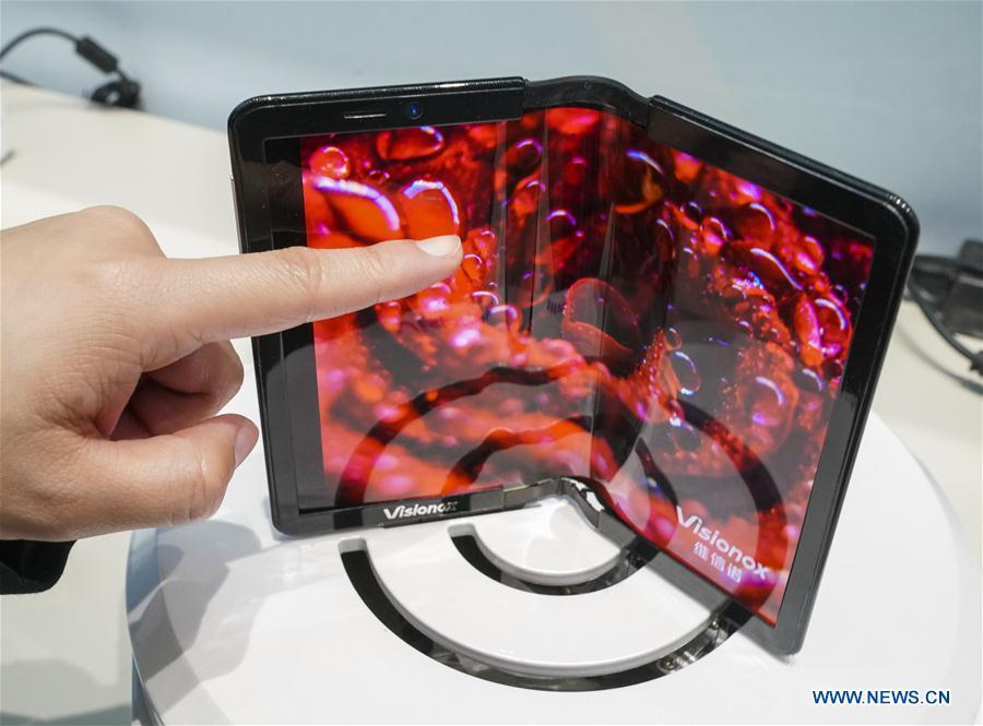 A staff member shows a phone with a foldable display screen during a major exhibition to commemorate the 40th anniversary of China\'s reform and opening-up at the National Museum of China in Beijing, capital of China, Nov. 24, 2018. (Xinhua/Yin Gang)
