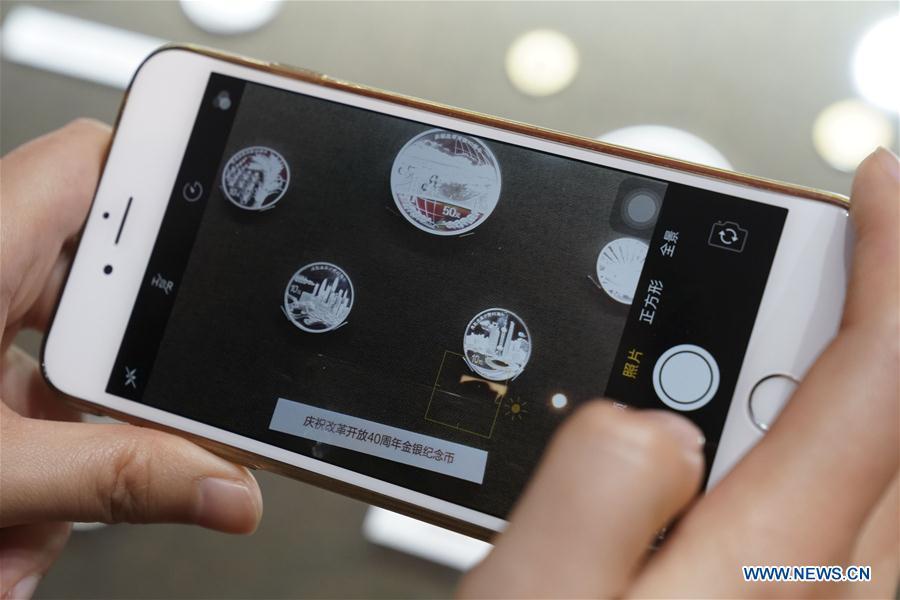 A visitor takes photos of commemorative coins displayed at a major exhibition to commemorate the 40th anniversary of China\'s reform and opening-up at the National Museum of China in Beijing, capital of China, Nov. 24, 2018. (Xinhua/Yin Gang)