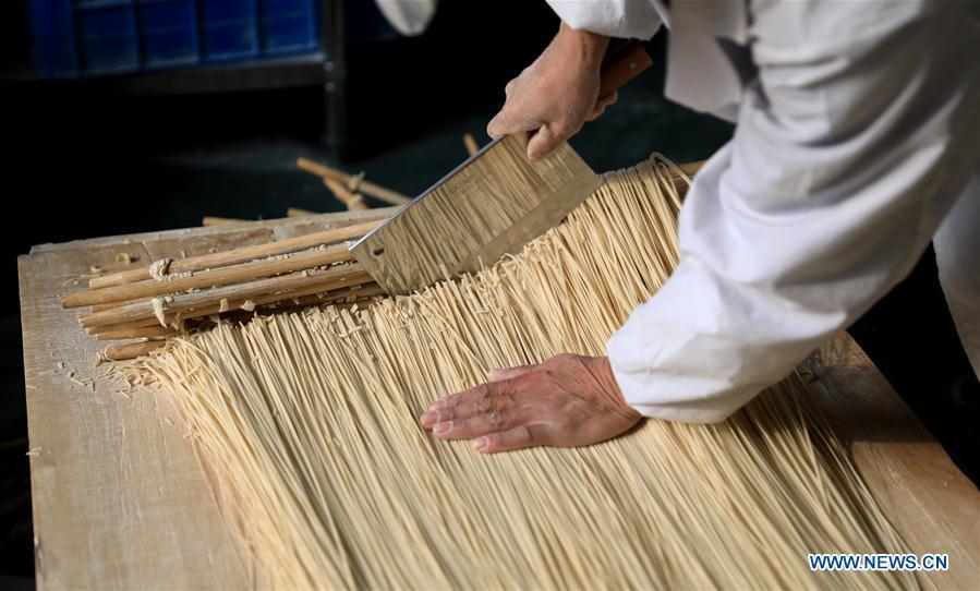 A worker makes noodles in a factory in Gengjiazhuang Village of Gaocheng District in Shijiazhuang, capital of north China\'s Hebei Province, Nov. 23, 2018. The fine dried noodle produced in Gongcheng, formerly article of tribute to the imperial family, is famous for its thin but hollow strings that is a result of more than ten working procedures. (Xinhua/Liang Zidong)