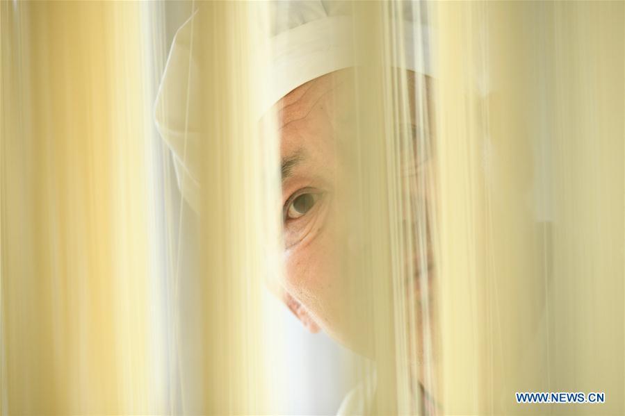 A worker examines noodles in a factory in Gengjiazhuang Village of Gaocheng District in Shijiazhuang, capital of north China\'s Hebei Province, Nov. 23, 2018. The fine dried noodle produced in Gongcheng, formerly article of tribute to the imperial family, is famous for its thin but hollow strings that is a result of more than ten working procedures. (Xinhua/Zheng Yaning)