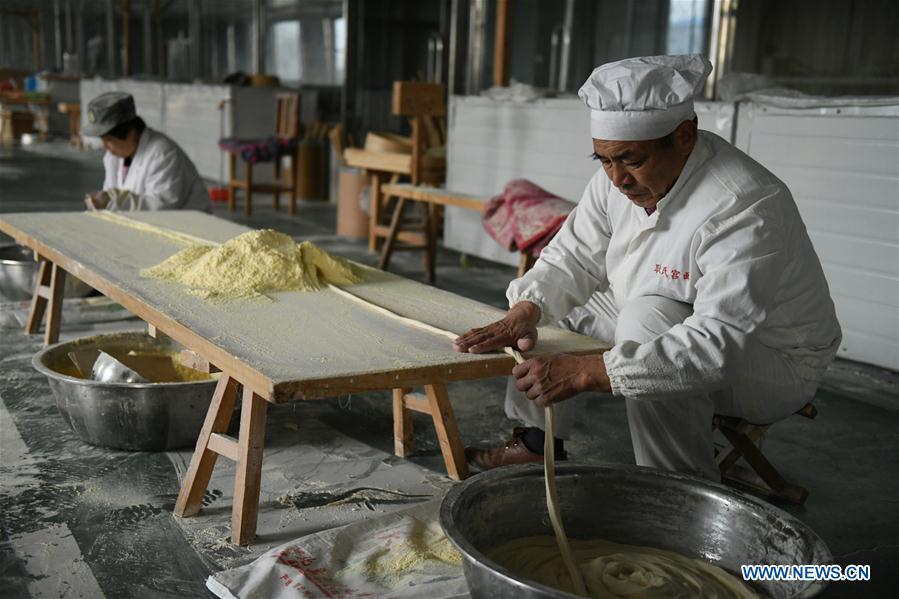 A worker makes noodles in a factory in Gengjiazhuang Village of Gaocheng District in Shijiazhuang, capital of north China\'s Hebei Province, Nov. 23, 2018. The fine dried noodle produced in Gongcheng, formerly article of tribute to the imperial family, is famous for its thin but hollow strings that is a result of more than ten working procedures. (Xinhua/Zheng Yaning)
