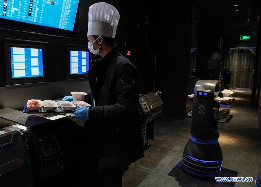 A delivery robot and a waiter work at the kitchen of a hot pot restaurant in Beijing, capital of China, Dec. 5, 2018. A hot pot restaurant which integrates artificial intelligence, big data management and smart robot service has attracted lots of consumers. After customers order their dishes with a tablet computer, robotic arms in the kitchen get all dishes ready and then the delivery robots sent the dishes to the tables. Workers in the kitchen control all the procedures and also monitor the data for better management. (Xinhua/Chen Junqing)