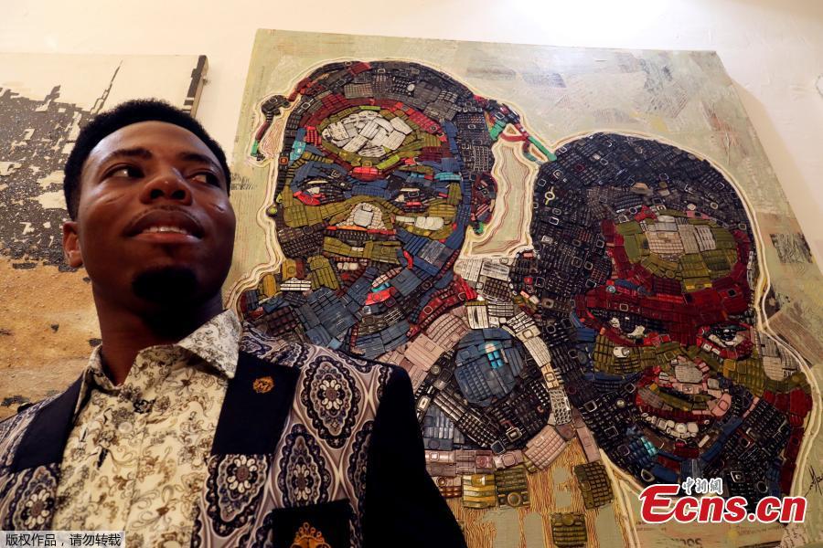 Desire Koffi, 24-year-old artist, poses next to his artwork during an exhibition in Abidjan, Ivory Coast, Dec. 1, 2018. Desire Koffi often walks through Koumassi, a popular district of Ivory Coast\'s main city Abidjan, to collect old mobile phones that he buys from people for 500 CFA francs ($0.8726) a pair. Back home, he dismantles the phones with a hammer to pull out the screens and keyboards. He uses them for his paintings. One can take him up to three or five days of work. (Photo/Agencies)