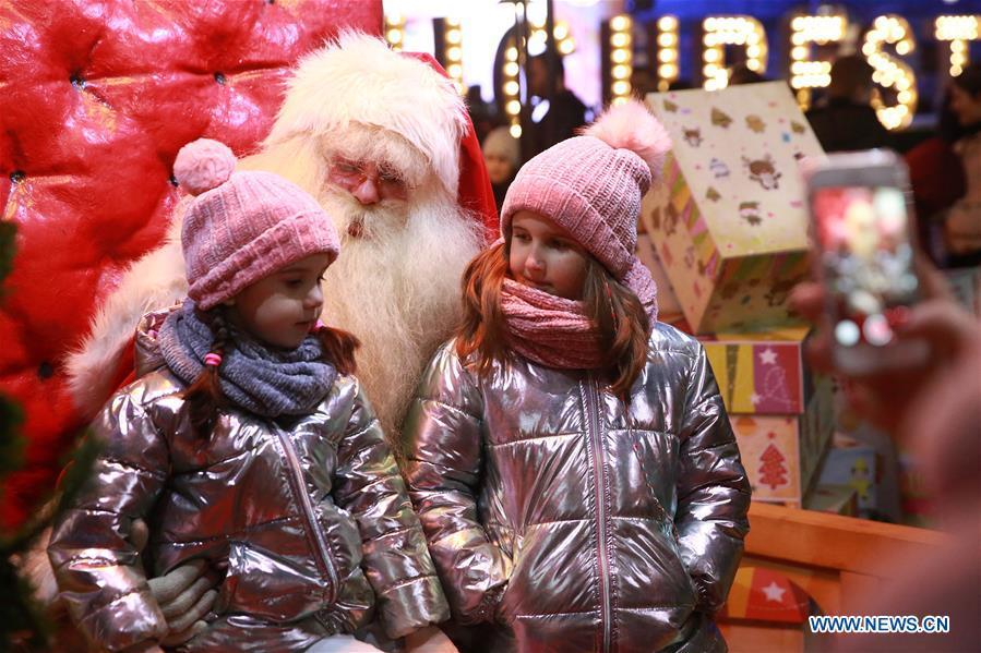 Two little girls pose for photos with a person in Santa Claus costume at Bucharest Winter Market at University Square, in Bucharest, Romania, on Dec. 24, 2018. (Xinhua/Gabriel Petrescu)