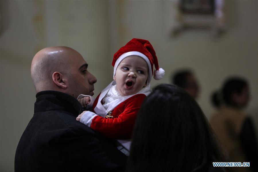 A baby in Santa Claus costume attends a Christmas mass at the Der Latin Church in Gaza City, on Dec. 24, 2018. (Xinhua/Stringer)