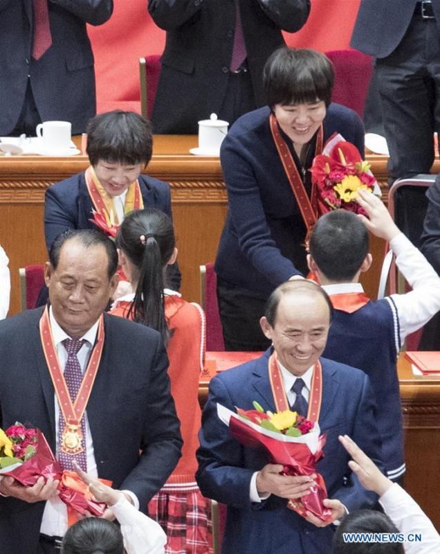 File photo taken on Dec. 18, 2018 shows Lang Ping (top R), head coach of China\'s women volleyball team, accepts bouquets presented by young pioneers during a grand gathering to celebrate the 40th anniversary of China\'s reform and opening-up at the Great Hall of the People in Beijing, capital of China. China\'s first-ever Olympic gold medalist Xu Haifeng, volleyball coach Lang Ping, and former NBA star Yao Ming were among the 100 people selected to be awarded for their contributions to the country\'s reform and opening-up. (Xinhua/Wang Ye)