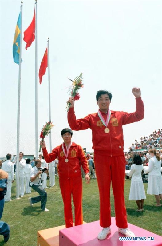 File photo taken on July 29, 1984 shows Chinese shooter Xu Haifeng (R) celebrates on the podium for men\'s pistol at the 10th Olympic Games in Los Angeles, the United States. It was China\'s first Olympic gold medal. China\'s first-ever Olympic gold medalist Xu Haifeng, volleyball coach Lang Ping, and former NBA star Yao Ming were among the 100 people selected to be awarded for their contributions to the country\'s reform and opening-up. (Xinhua/Guan Tianyi)