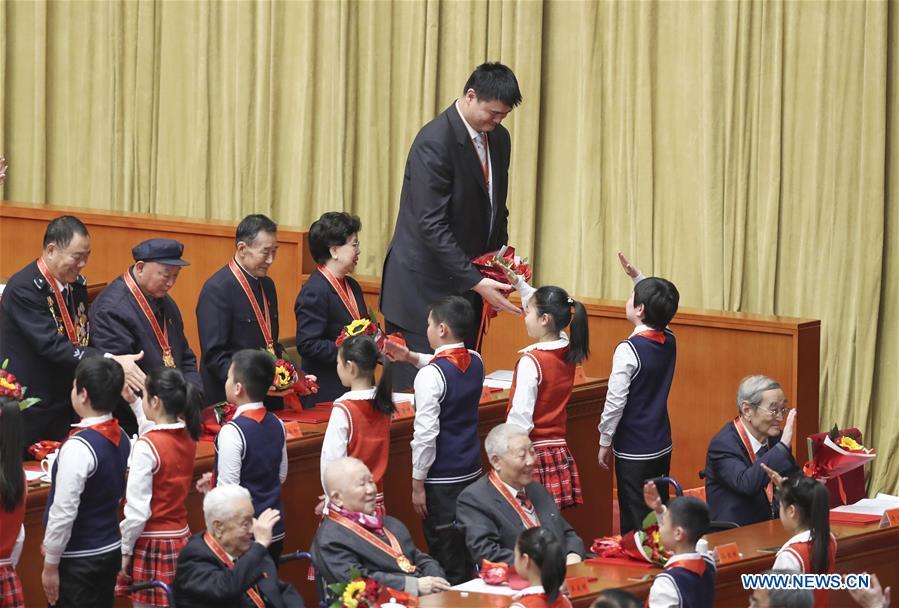 File photo taken on Dec. 18, 2018 shows Yao Ming (top), president of the Chinese Basketball Association (CBA) accepts bouquets presented by young pioneers during a grand gathering to celebrate the 40th anniversary of China\'s reform and opening-up at the Great Hall of the People in Beijing, capital of China. China\'s first-ever Olympic gold medalist Xu Haifeng, volleyball coach Lang Ping, and former NBA star Yao Ming were among the 100 people selected to be awarded for their contributions to the country\'s reform and opening-up. (Xinhua/Yin Gang)