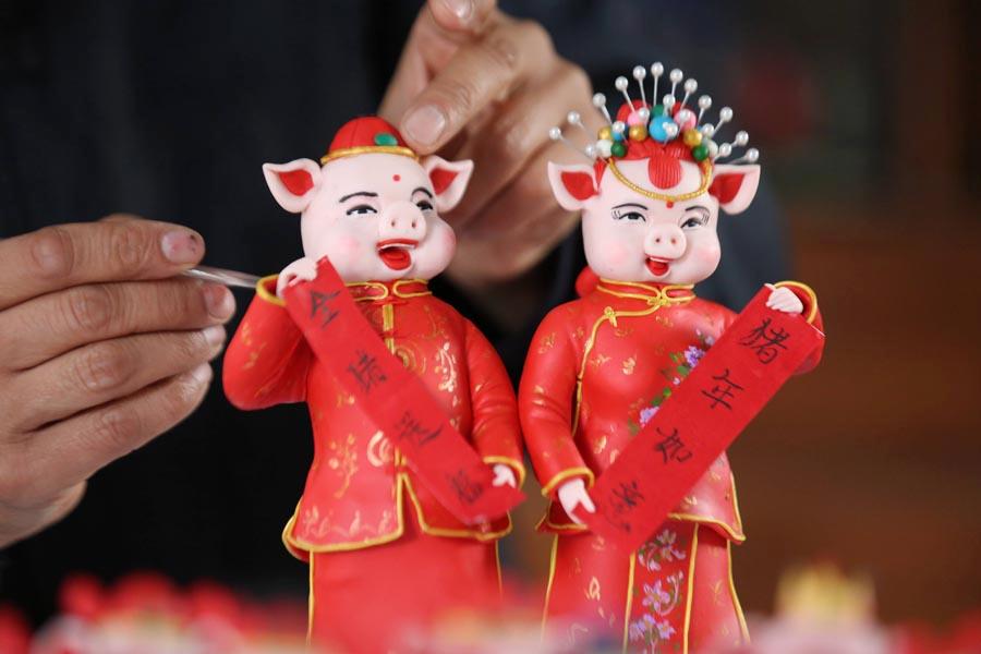 Chinese people expect loads of pig-themed decorations and items as the lunar Year of the Pig draws near. This photo taken on Jan. 8, 2019 shows a pair of dough figurines of pigs holding couplets to greet people for an auspicious new year. They were made by craftsman Zuo Ansheng in Linyi city in East China\'s Shandong Province. (Photo/Asianewsphoto)