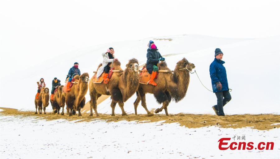 Tourists ride camels at the Crescent Spring and Singing-Sand Dunes scenic spot in Dunhuang City, Northwest China\'s Gansu Province, Jan. 19, 2019, after the area\'s first snow for the year. (Photo: China News Service/Wang Binyin)