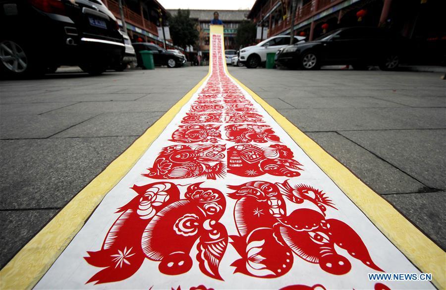 Folk artist Shi Hongxia shows a pig-themed paper cutting artwork in Tengzhou City, east China\'s Shandong Province, Jan. 31, 2019. Shi has spent two months to create the artwork, which is 9 meters long and features 100 pig figures, to greet the coming of the Year of the Pig. (Xinhua/Sun Zhongzhe)