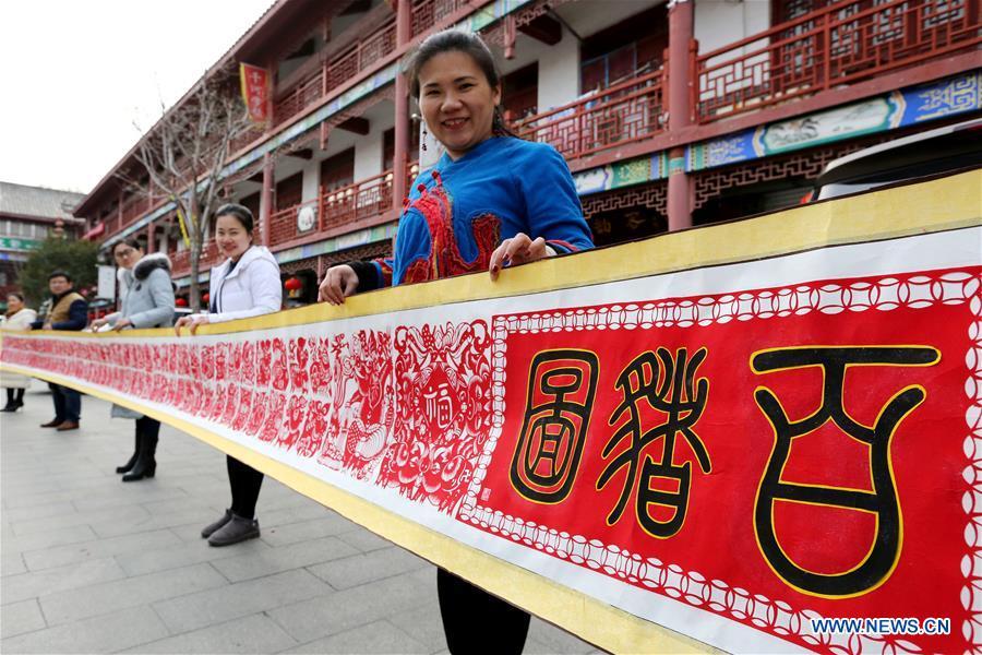 Folk artist Shi Hongxia (1st R) shows a pig-themed paper cutting artwork in Tengzhou City, east China\'s Shandong Province, Jan. 31, 2019. Shi has spent two months to create the artwork, which is 9 meters long and features 100 pig figures, to greet the coming of the Year of the Pig. (Xinhua/Sun Zhongzhe)