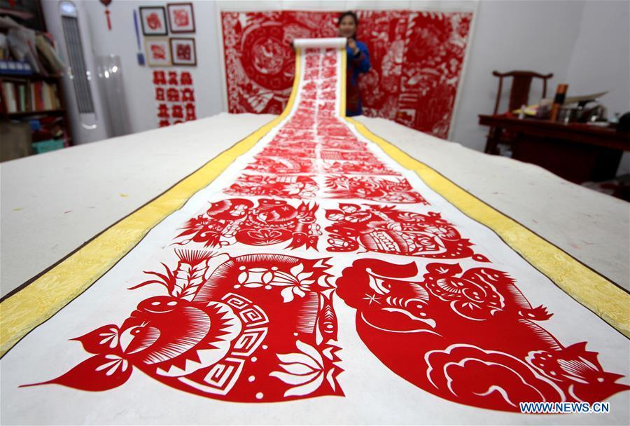 Folk artist Shi Hongxia shows a pig-themed paper cutting artwork at home in Tengzhou City, east China\'s Shandong Province, Jan. 31, 2019. Shi has spent two months to create the artwork, which is 9 meters long and features 100 pig figures, to greet the coming of the Year of the Pig. (Xinhua/Sun Zhongzhe)