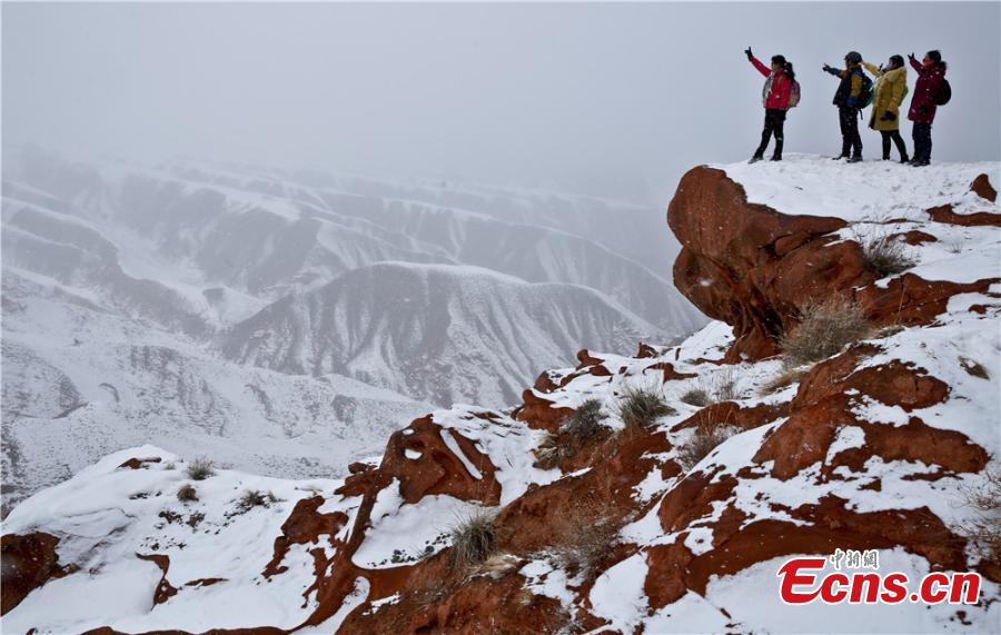 Tourists visit the snow-covered Danxia landform in Sunan Yugur Autonomous County, Northwest China\'s Gansu Province during the Spring Festival holiday. The Danxia landform is a unique type of geomorphology formed from red-colored sandstone and characterized by steep cliffs. (Photo: China News Service/Wang Jiang)