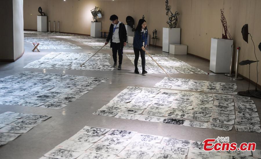 Judges use bamboo sticks to help them review paintings by applicants to the Shandong University of Arts in Jinan City, Shandong Province, Feb. 28, 2019. More than 10,000 paintings were placed in a corridor for judges to grade. (Photo: China News Service/Zhang Yong)