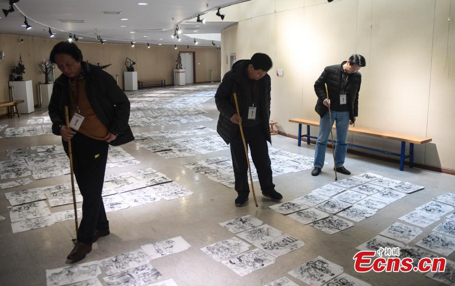 Judges use bamboo sticks to help them review paintings by applicants to the Shandong University of Arts in Jinan City, Shandong Province, Feb. 28, 2019. More than 10,000 paintings were placed in a corridor for judges to grade. (Photo: China News Service/Zhang Yong)
