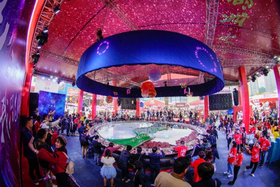 Diners eat from a huge hotpot at a festival in Chongqing. The four-day event attracted thousands of diners and enterprises (Photo/Xinhua)
Local authorities keep close eye on spicy cuisine\'s development

In the recent Chinese science fiction blockbuster The Wandering Earth, astronaut Liu Peiqiang tells Russian cosmonaut Makarov that he will invite him to have hotpot in Chongqing after they return to Earth. But Makarov dies before he can make the trip to China.

Although the death scene in the movie is upsetting, fans of this strongly flavored and oily local dish are delighted to see that their favorite food has become well-known-even in space.

Chongqing hotpot has become hugely popular in recent years, especially since the release of the food documentary series A Bite of China II five years ago.

It seems as though there are Chongqing hotpot restaurants in every Chinese city, even though most people in northern and coastal regions have not been big consumers of chili peppers in the past.

Many people believe the cuisine not only reflects the character of Chongqing\'s people but has also become a driving force of the local economy.

Hotpot cooking is believed to have spread through northern China during the Tang Dynasty (618-907). By the time of the Qing Dynasty (1644-1911), it was popular nationwide.

Although there are many regional variations, the one from Chongqing differs from other styles with its numbing, spicy soup base and special meats and sauces.

All hotpot cuisine is basically the same. While the soup simmers over a flame, meat and vegetables are placed into the pot to cook, and diners can select the items when they are ready to eat.

But Chongqing hotpot has the strongest flavor, with beef tallow, large quantities of chili and Sichuan pepper. The three must-have varieties are ox stomach, duck intestine and large pig or ox artery.

Although there is no evidence of how the cuisine originated, many believe that hotpot emerged from porters\' food in the late 19th century.