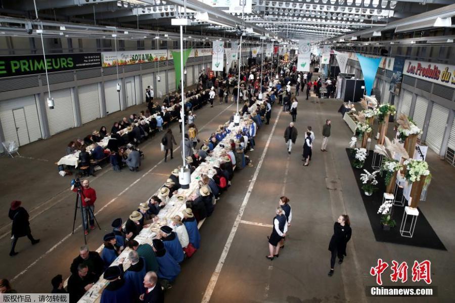 Participants attend a lunch served on a 401.22-meter-long table in the fruit and vegetable pavilion at the Rungis International Food Market during an event near Paris, France on March 17 celebrating the market’s 50th anniversary, which also aims to set a Guinness World Record.(Photo/Agencies)