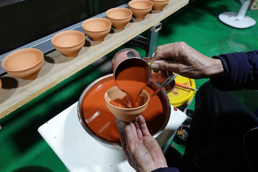 Wu Lizhu, inheritor of the workmanship of Jianzhan teaware, glazes a piece of porcelain at his workshop in Jianyang District of Nanping City, south China\'s Fujian Province, March 28, 2019. Jianzhan teaware, a well-known Chinese porcelain originated in Jianyang, dates back to more than 1,000 years ago in Song dynasty (960-1279). It was the best teaware for scholars and literati to use during that time in tea competitions. Jianzhan teawares are known for their variability. Glazes can range in color from dark plum to yellow, green, and blue. During the heating and cooling processes, iron element in the clay can migrate within the glaze to form surface crystals in rich and glossy colors, as in the \