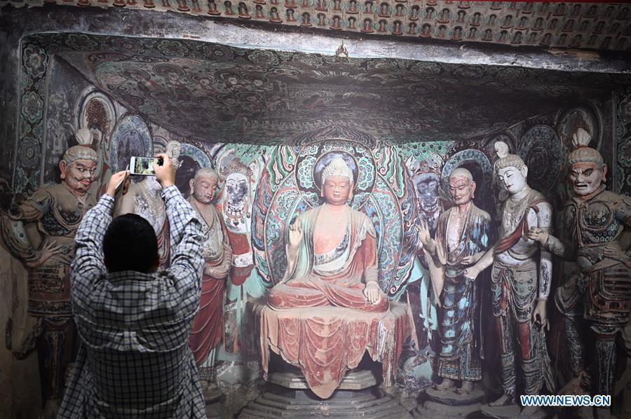 A visitor takes photos of a fresco during a Dunhuang fresco itinerant exhibition in Yunnan University in Kunming, southwest China\'s Yunnan Province, April 10, 2019. A Dunhuang fresco itinerant exhibition, with the participation of nearly 50 frescoes, was held in Yunnan University in Kunming Wednesday. (Xinhua/Qin Qing)