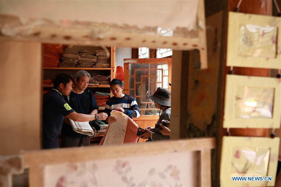 Wang Xingwu (2nd L), a paper maker, introduces his paper product to Japanese tourists at a workshop in Shiqiao Village of Danzhai County, southwest China\'s Guizhou Province, April 24, 2019. Wang Xingwu, 53, a national intangible cultural heritage inheritor in papermaking, learned the papermaking technique from his family as a child. Besides exerting the old papermaking technique to its full potential, Wang keeps raising product quality and improving the making procedure. With the involvement of plants in the papermaking process, he has created more than 160 kinds of patterned papers and paper crafts. He also develops a kind of handmade white paper more suitable for writing calligraphy and painting. (Xinhua/Huang Xiaohai)