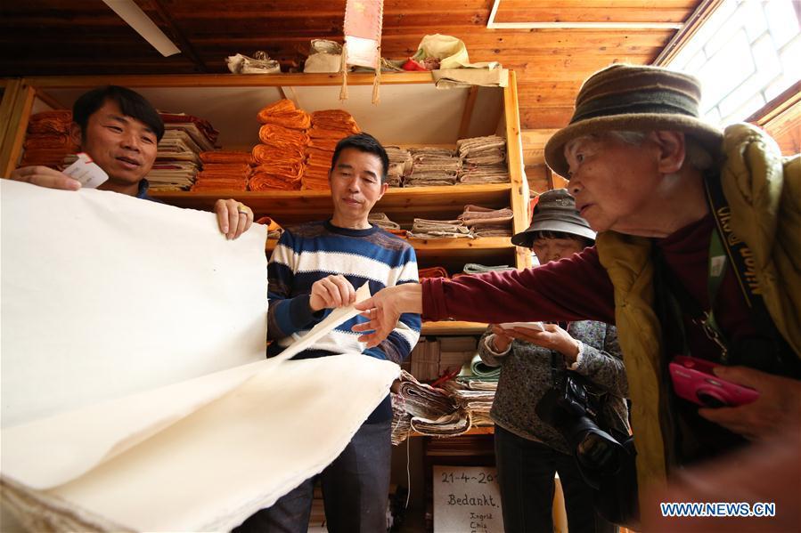 Wang Xingwu (2nd L), a papermaker, introduces his paper product to Japanese tourists at a workshop in Shiqiao Village of Danzhai County, southwest China\'s Guizhou Province, April 24, 2019. Wang Xingwu, 53, a national intangible cultural heritage inheritor in papermaking, learned the papermaking technique from his family as a child. Besides exerting the old papermaking technique to its full potential, Wang keeps raising product quality and improving the making procedure. With the involvement of plants in the papermaking process, he has created more than 160 kinds of patterned papers and paper crafts. He also develops a kind of handmade white paper more suitable for writing calligraphy and painting. (Xinhua/Huang Xiaohai)
