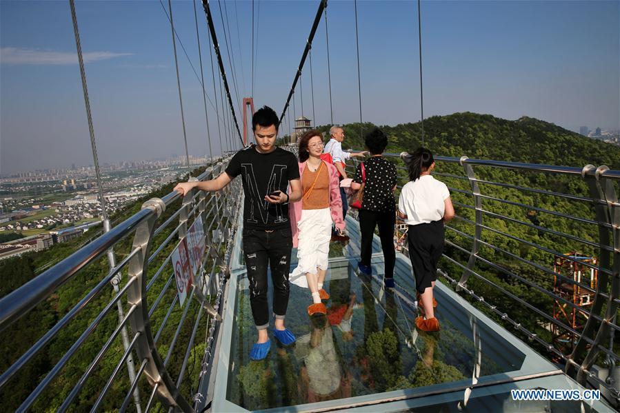 Tourists walk on a glass bridge at the Huaxi World Adventure Park in Huaxi Village of Jiangyin City, east China\'s Jiangsu Province, May 4, 2019. The 518-meter-long glass bridge hangs more than 100 meters above ground level at the park. It is made of panes of 35-mm-thick glass. Each glass can hold a maximum weight of 4.7 tonnes. Around 2,600 people can cross the bridge at a time. (Xinhua/Xu Congjun)