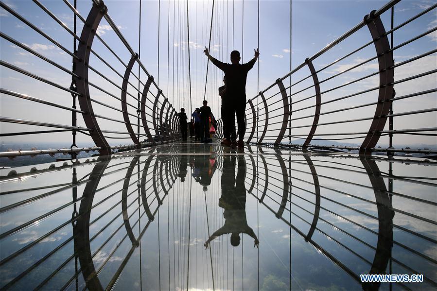 Tourists walk on a glass bridge at the Huaxi World Adventure Park in Huaxi Village of Jiangyin City, east China\'s Jiangsu Province, May 4, 2019. The 518-meter-long glass bridge hangs more than 100 meters above ground level at the park. It is made of panes of 35-mm-thick glass. Each glass can hold a maximum weight of 4.7 tonnes. Around 2,600 people can cross the bridge at a time. (Xinhua/Xu Congjun)