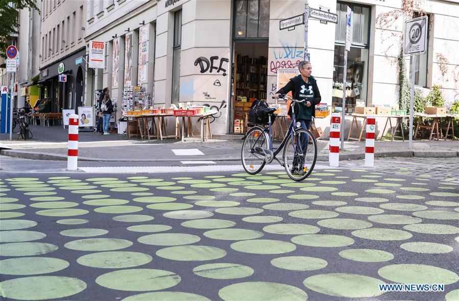 A pedestrian with a bicycle walks across a green dotted street area in Bergmann Street of Kreuzberg, southern Berlin, Germany, on May 7, 2019. The green dots, part of new street signals in Berlin, are applied as a trial at a part of Bergmann Street with a speed limit of 20km/h, aiming to induce vehicles to drive with restricted speed. (Xinhua/Shan Yuqi)
