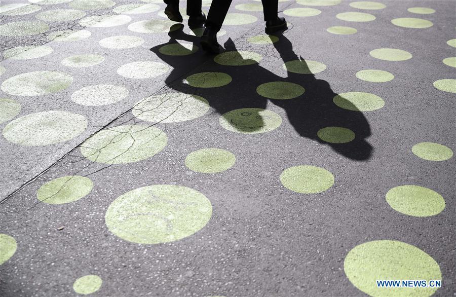 Two pedestrians walk across a green dotted street area in Bergmann Street of Kreuzberg, southern Berlin, Germany, on May 7, 2019. The green dots, part of new street signals in Berlin, are applied as a trial at a part of Bergmann Street with a speed limit of 20km/h, aiming to induce vehicles to drive with restricted speed. (Xinhua/Shan Yuqi)