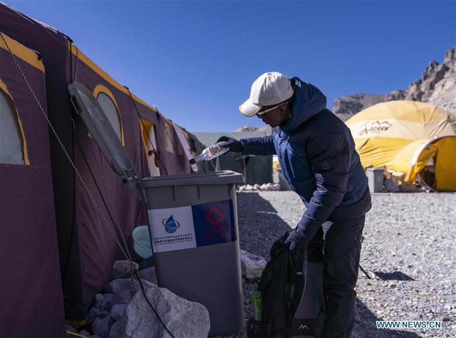 The mountain guide Sonam Tsering throws the garbage into the trash can at the base camp of the northern face of Mount Qomolangma in southwest China\'s Tibet Autonomous Region, April 26, 2019. Every year, for a few weeks, hundreds of climbers and supporting personnel come to the base camp of the northern face of Mount Qomolangma, trying to reach the summit of the tallest and most famous mountain in the world. Before starting climbing, they need to hike several times between elevations from 5,000 meters to 7,000 meters, giving their bodies some time to adapt. When this process is over, it\'s all up to the weather. The base camp is a popular place to wait for the window. Among the six camps on the northern face, the base camp at an altitude of 5,200 meters is the furthest cars can reach and therefor the most equipped. Besides food and accommodation, climbers can also enjoy tea and massage. They can also play football on perhaps the highest field. There\'s even a simple gym in the camp. Environmental protection is a priority here. Garbage sacks are given to each climbing team. Special containers are put in every camp to collect trash and sewage. The collected trash must be treated 100 kilometers away, and the only road is a zigzagging track. It is not trucks, but yaks that are generally used to make the journey. Actually yaks are vital on the mountain. Beyond the base camp, yak is the only reliable transport. (Xinhua/Sun Fei)