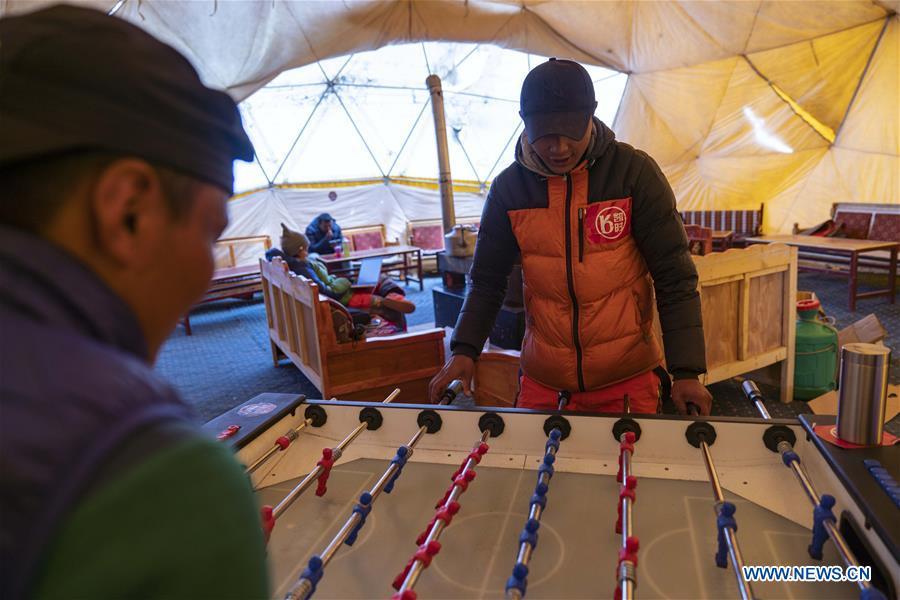 Climbers play table football in the tent of the Chinese mountaineering team at the base camp of the northern face of Mount Qomolangma in southwest China\'s Tibet Autonomous Region, April 25, 2019. Every year, for a few weeks, hundreds of climbers and supporting personnel come to the base camp of the northern face of Mount Qomolangma, trying to reach the summit of the tallest and most famous mountain in the world. Before starting climbing, they need to hike several times between elevations from 5,000 meters to 7,000 meters, giving their bodies some time to adapt. When this process is over, it\'s all up to the weather. The base camp is a popular place to wait for the window. Among the six camps on the northern face, the base camp at an altitude of 5,200 meters is the furthest cars can reach and therefor the most equipped. Besides food and accommodation, climbers can also enjoy tea and massage. They can also play football on perhaps the highest field. There\'s even a simple gym in the camp. Environmental protection is a priority here. Garbage sacks are given to each climbing team. Special containers are put in every camp to collect trash and sewage. The collected trash must be treated 100 kilometers away, and the only road is a zigzagging track. It is not trucks, but yaks that are generally used to make the journey. Actually yaks are vital on the mountain. Beyond the base camp, yak is the only reliable transport. (Xinhua/Sun Fei)