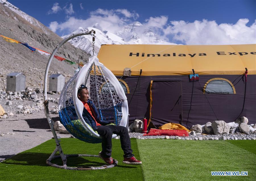 The mountain guide Sonam Tsering takes a break at the base camp of the northern face of Mount Qomolangma in southwest China\'s Tibet Autonomous Region, April 26, 2019. Every year, for a few weeks, hundreds of climbers and supporting personnel come to the base camp of the northern face of Mount Qomolangma, trying to reach the summit of the tallest and most famous mountain in the world. Before starting climbing, they need to hike several times between elevations from 5,000 meters to 7,000 meters, giving their bodies some time to adapt. When this process is over, it\'s all up to the weather. The base camp is a popular place to wait for the window. Among the six camps on the northern face, the base camp at an altitude of 5,200 meters is the furthest cars can reach and therefor the most equipped. Besides food and accommodation, climbers can also enjoy tea and massage. They can also play football on perhaps the highest field. There\'s even a simple gym in the camp. Environmental protection is a priority here. Garbage sacks are given to each climbing team. Special containers are put in every camp to collect trash and sewage. The collected trash must be treated 100 kilometers away, and the only road is a zigzagging track. It is not trucks, but yaks that are generally used to make the journey. Actually yaks are vital on the mountain. Beyond the base camp, yak is the only reliable transport. (Xinhua/Sun Fei)